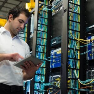 A man in white shirt holding a tablet near wires.